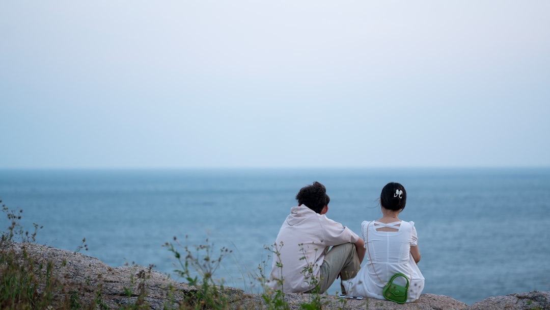 two people sitting on a rock looking out at the ocean