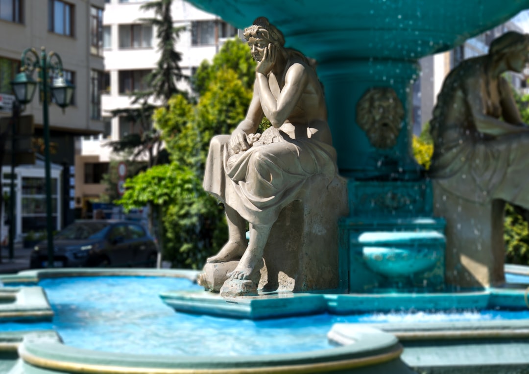 Statues adorn a beautiful teal fountain in the city.